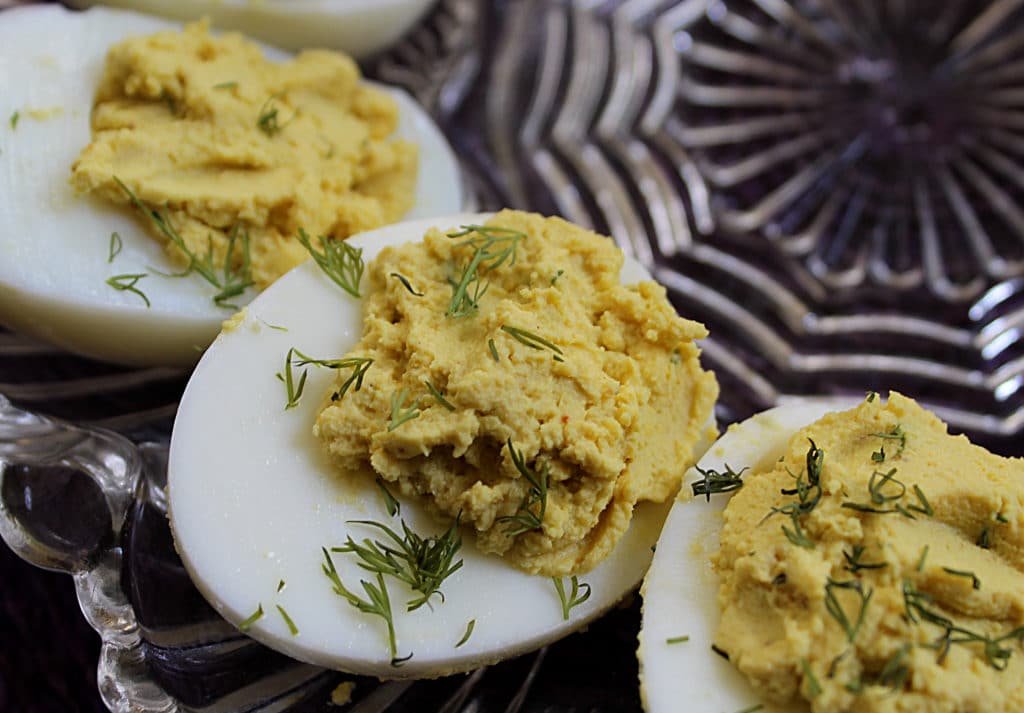Curry and fresh dill deviled egg halves on a decorative plate