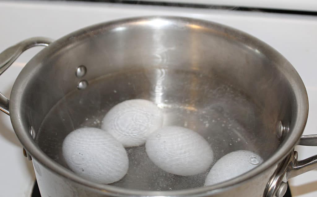 raw eggs just starting to boil in a pot on the stove
