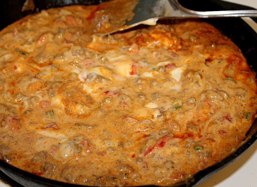 Spicy Rotel Sausage Cheese Dip stirring on the stove in a cast iron skillet