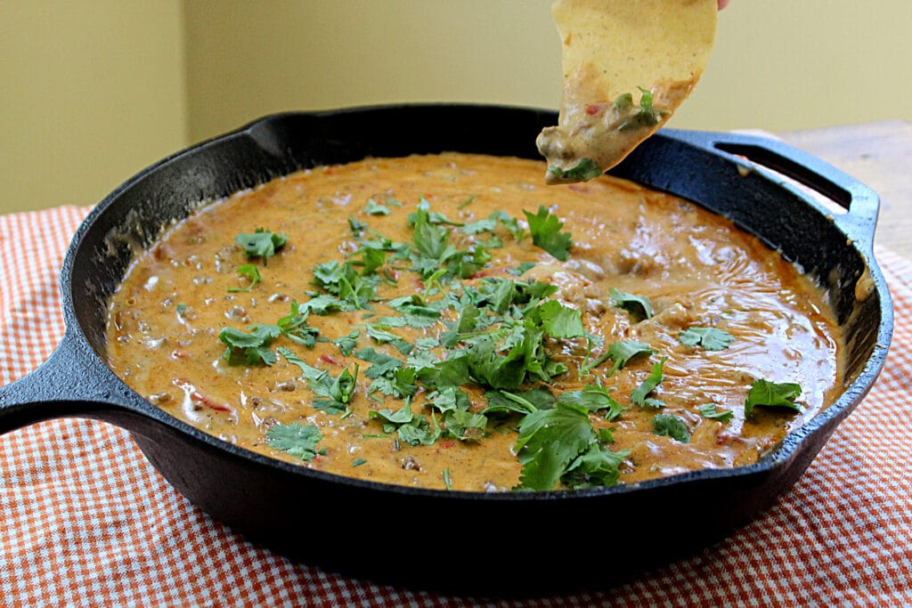 Spicy Rotel Sausage Cheese Dip with cilantro in a cast iron skillet on a tortilla chip