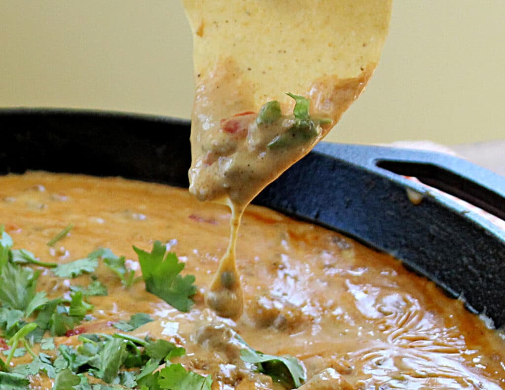 Spicy Rotel Sausage Cheese Dip with cilantro in a cast iron skillet on a tortilla chip close up