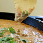 Spicy Rotel Sausage Cheese Dip with cilantro in a cast iron skillet on a tortilla chip close up