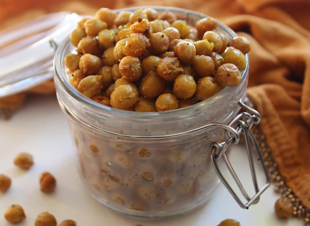 Close up of curry crunchy chickpeas in a class jar on a white table