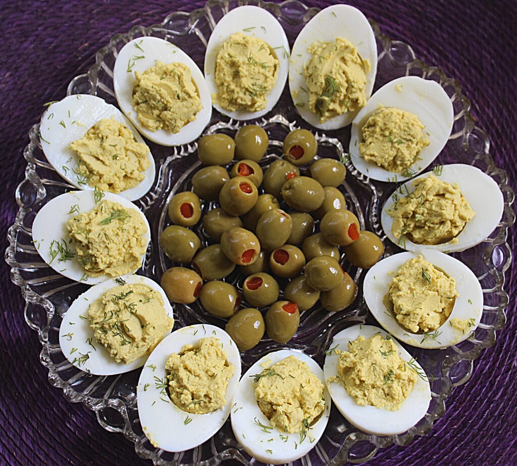 deviled eggs with curry and fresh dill on a glass egg plate with green olives in the middle