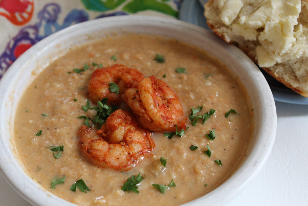 Cauliflower Shrimp Bisque with seasoned shrimp and parsley on top in a white bowl with buttered bread
