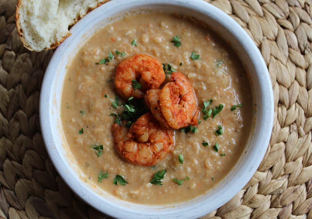overhead of Cauliflower Shrimp Bisque in a white bowl on a tan woven place mat
