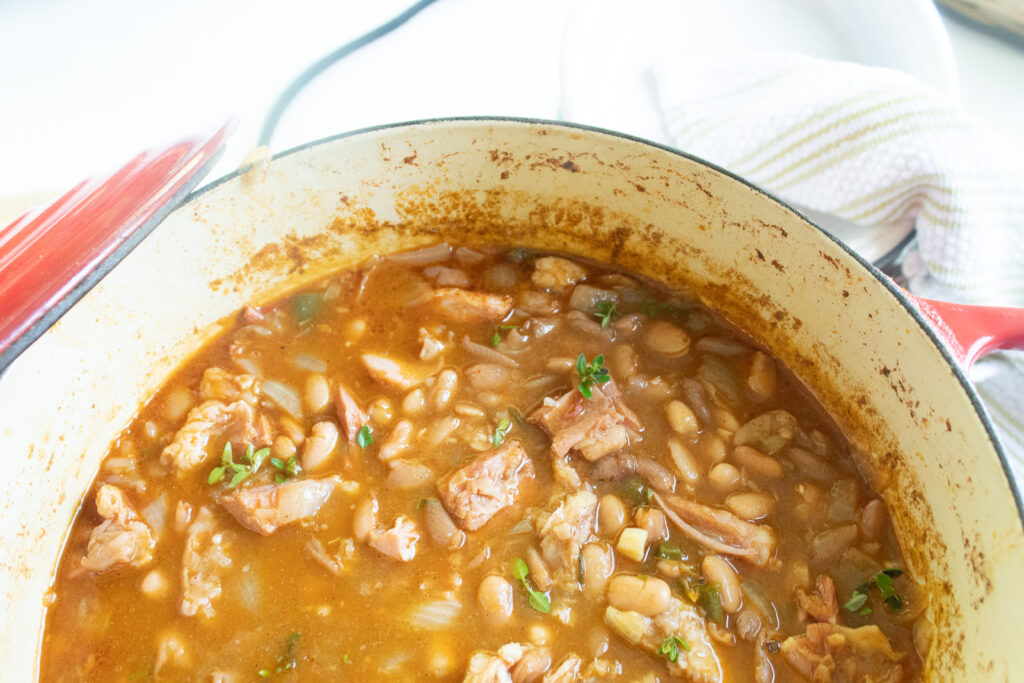 savory pinto beans and ham in a large red dutch oven with fresh herbs.