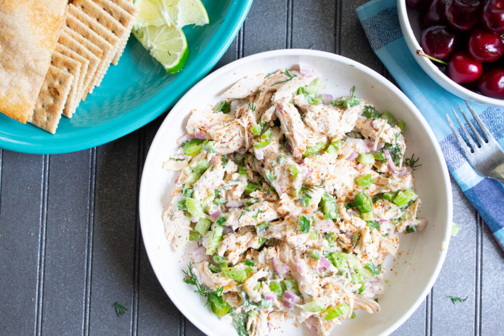 overhead of healthy chicken salad in a white bowl with fresh cherries and crackers on the side