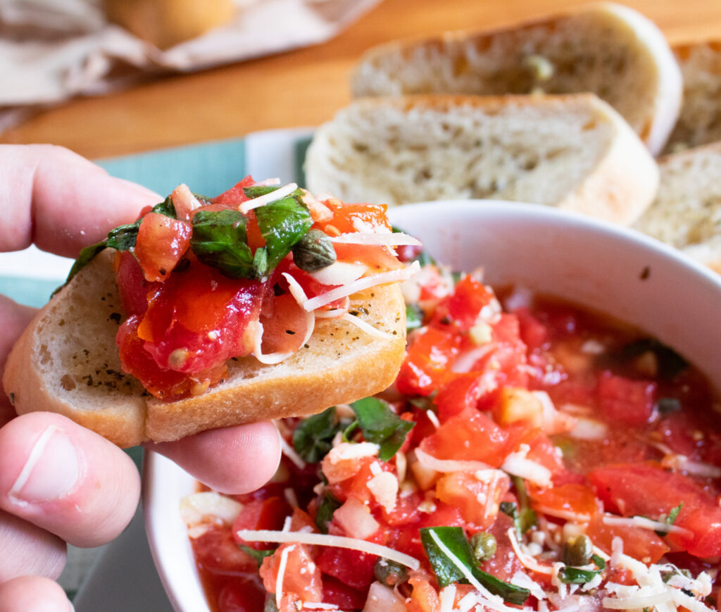 close up on fresh garden tomato basil bruschetta on a piece of garlic bread over a big bowl ofgarden fresh tomato basil bruschetta