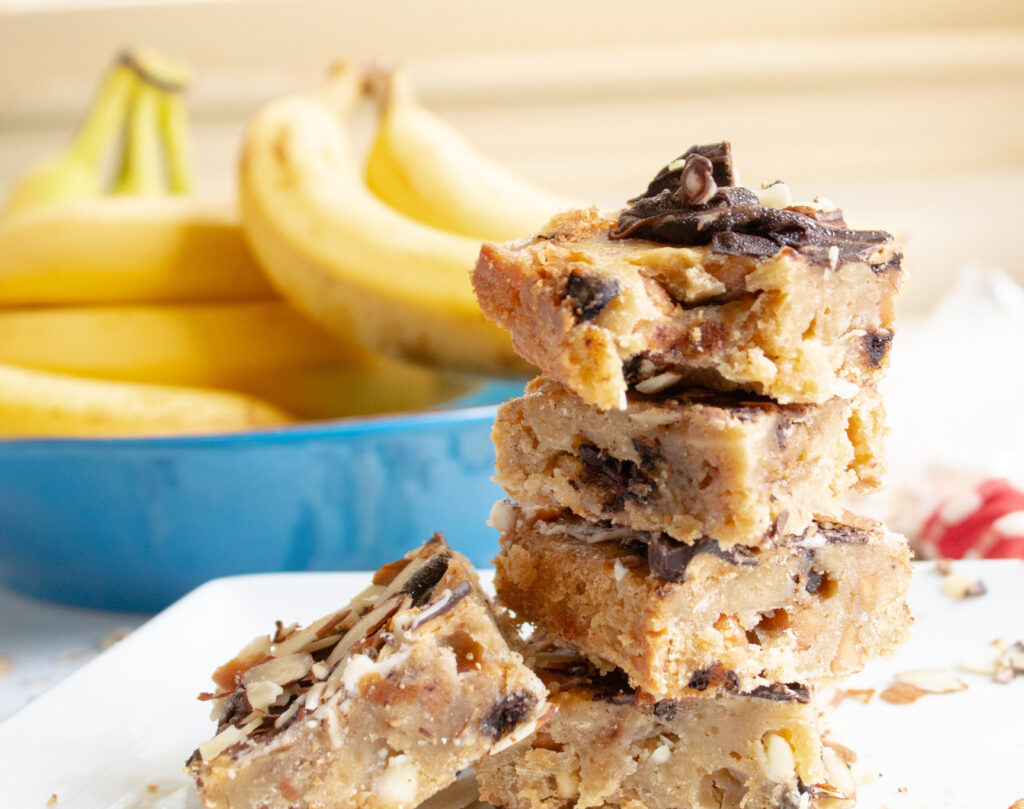 Stack of Blondie Banana Brownies with bananas in the background