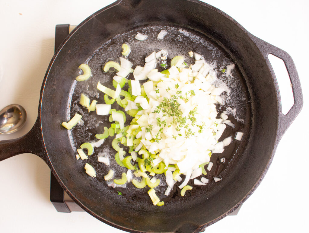 overhead of celery, onion, thyme and butter in a skillet