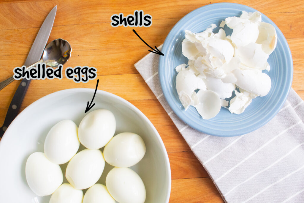 Shelled eggs with shells in a white bowl and on a grey and white dish towel