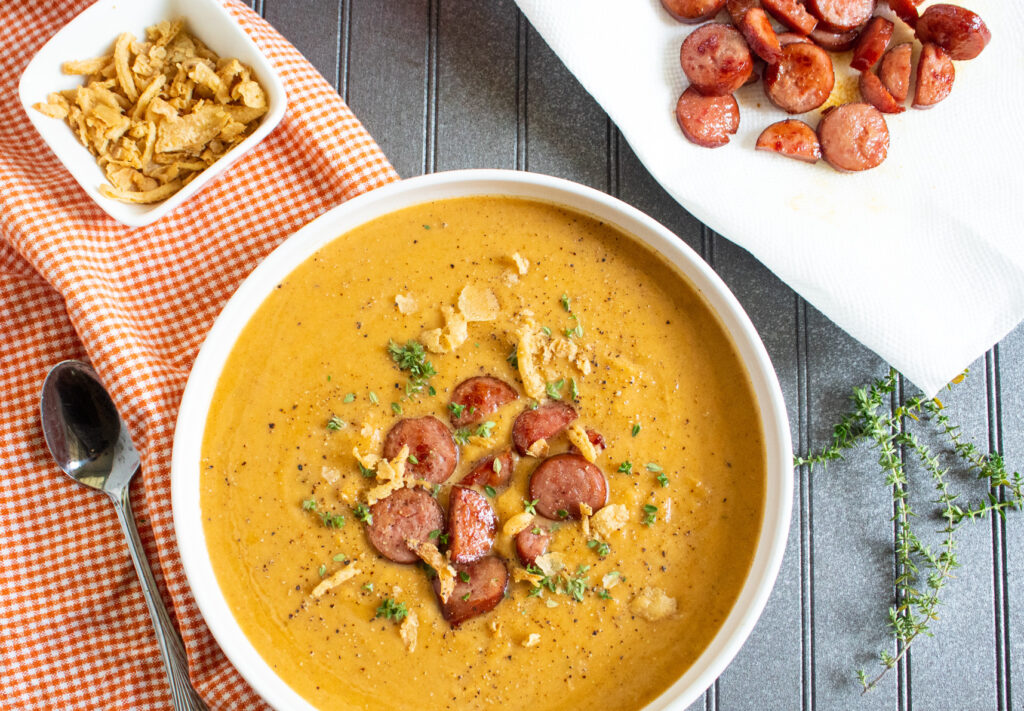 overhead picture of butternut squash soup with sausage with french fried onions and sausage in a bowl and on a plate. 