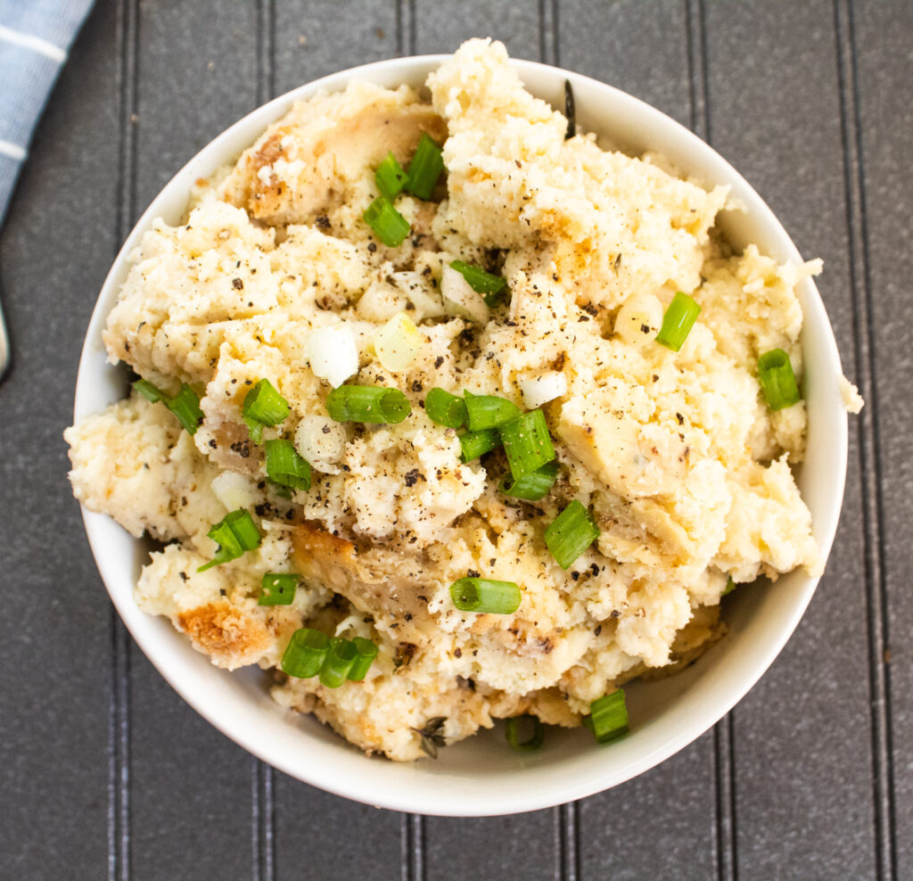 overhead mashed potato cauliflower casserole with green onions on top in a white bowl