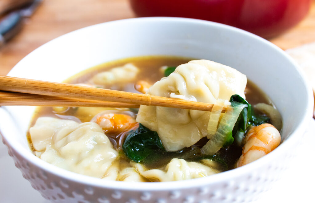 close up of easy 30 minute wonton soup in a white bowl with chop sticks