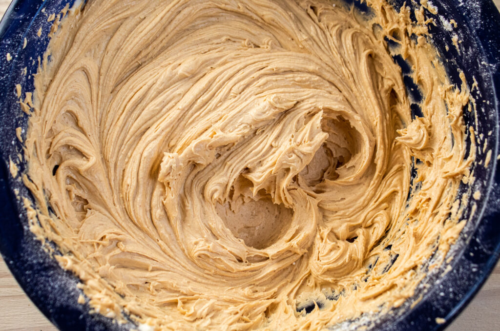 Mixed and swirled peanut butter frosting in a blue glas mixing bowl.