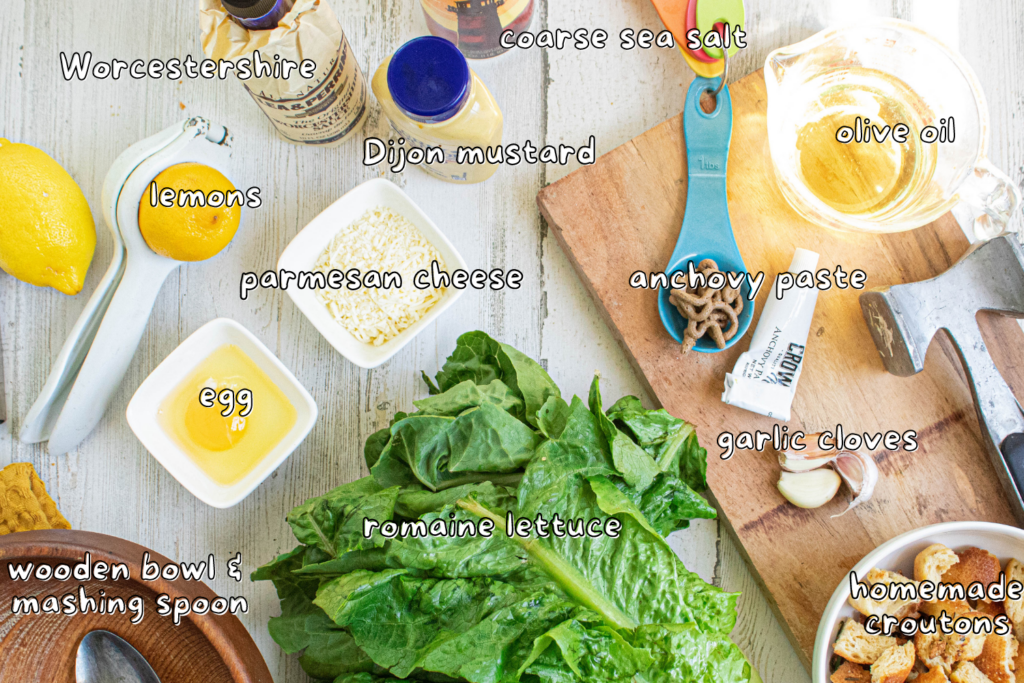 Caesar salad ingredients on a white wood table with labels for ingredients