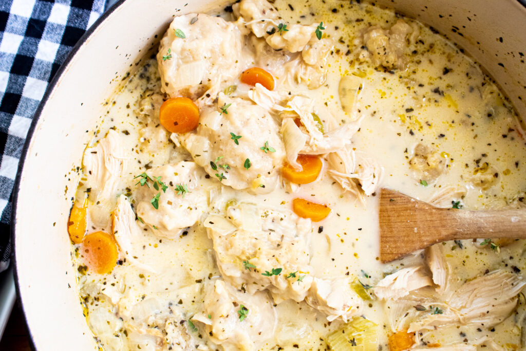 chicken and dumplings in a white dutch oven with a wooden spoon