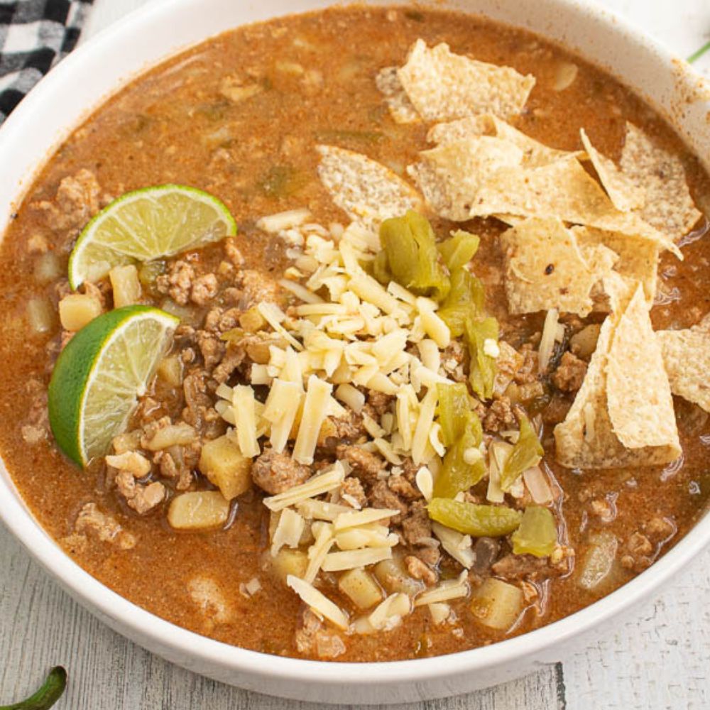 close overhead of green chili ground turkey soup with tortilla chips, cheese, green chilis, and lime slices.