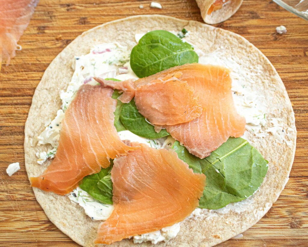 Tortilla with cream cheese mixture smeared on with a layer of fresh spinach and smoked salmon slices on top.