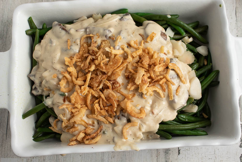 Blanched green beans and sliced water chestnuts in a white rectangle casserole dish with cream sauce and french fried onions on top.