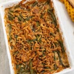 Cooked green bean casserole in a white rectangle casserole dish with unbaked canned french fried onions on top.