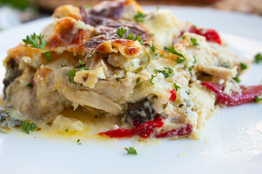 Side view of single serving of creamy white lasagna with spinach and red onions on a white plate.