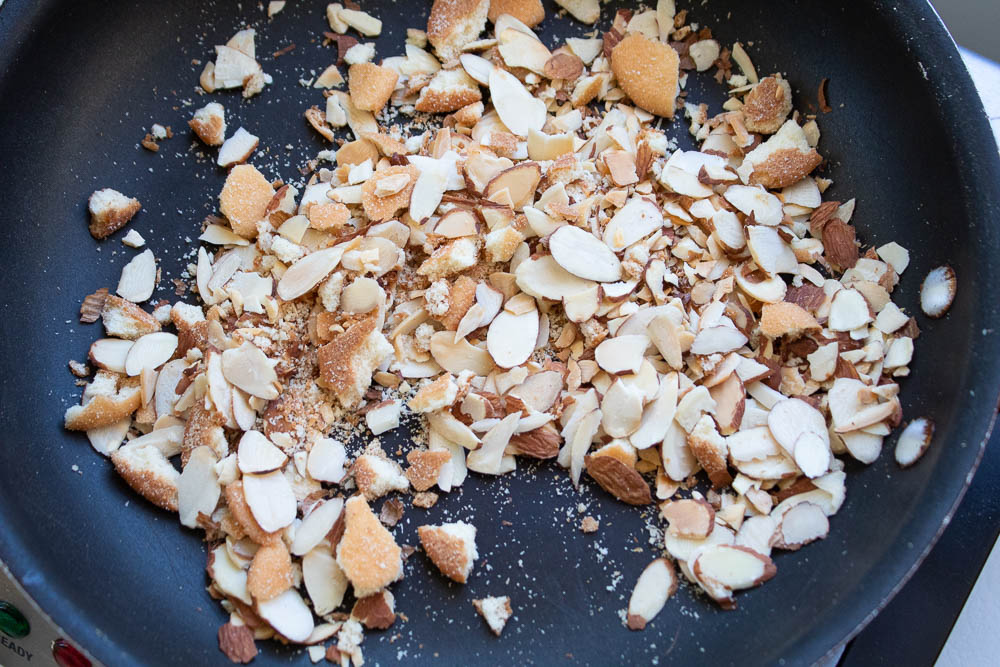 Toasted almond slices and cookie crumbs in a black non stick skillet.