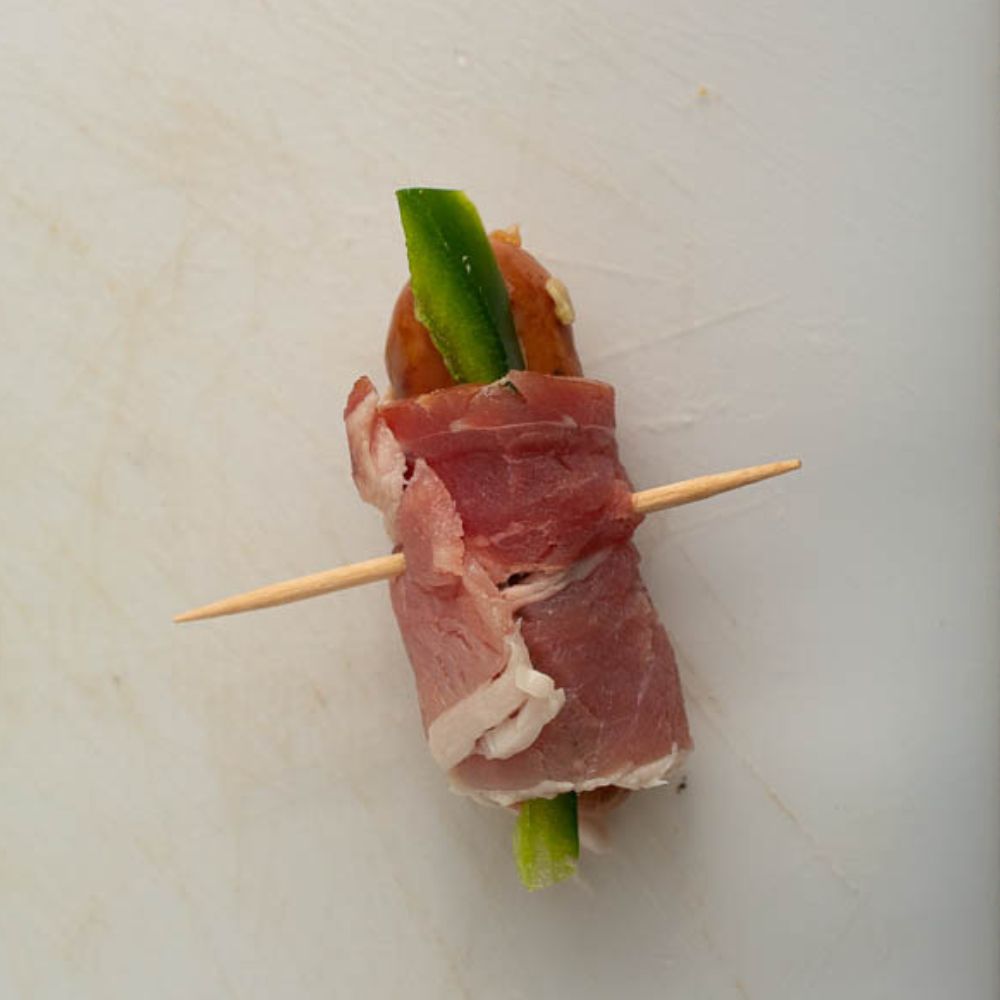 Uncooked bacon wrapped smokie and jalapeno with a toothpick inserted.